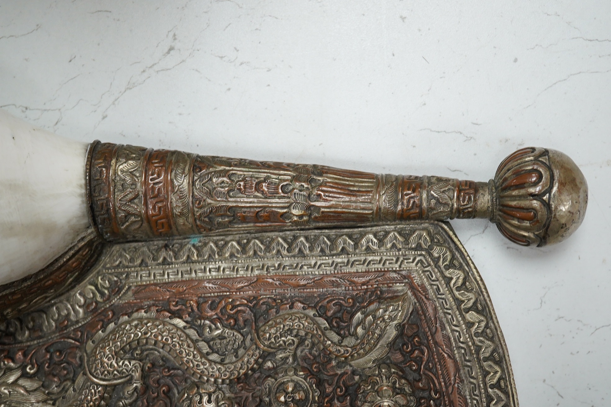 A Tibetan repoussé work cowrie shell trumpet, early 20th century, set with a cabochon, 37cm high. Condition - fair to good